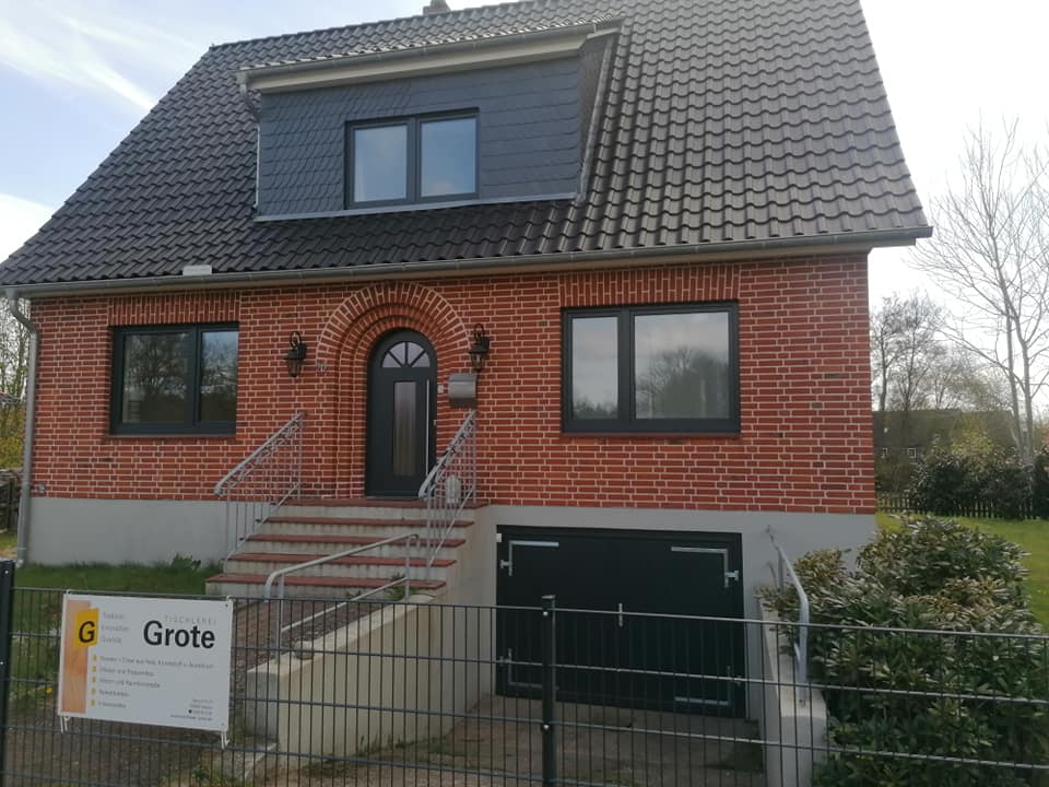 Sanierte Klinkerfassade eines Einfamilienhauses mit neuen Fenstern und Bauschild der Tischlerei Grote