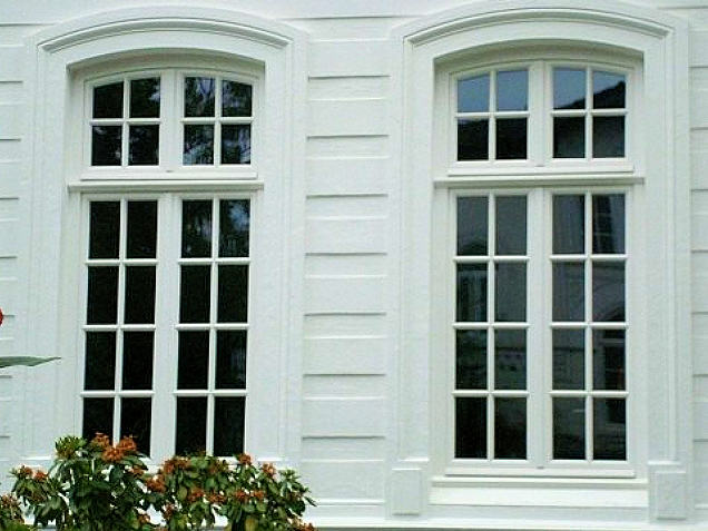 Weiße Rundbogenfenster mit Sprossen in einer hellen Fassade