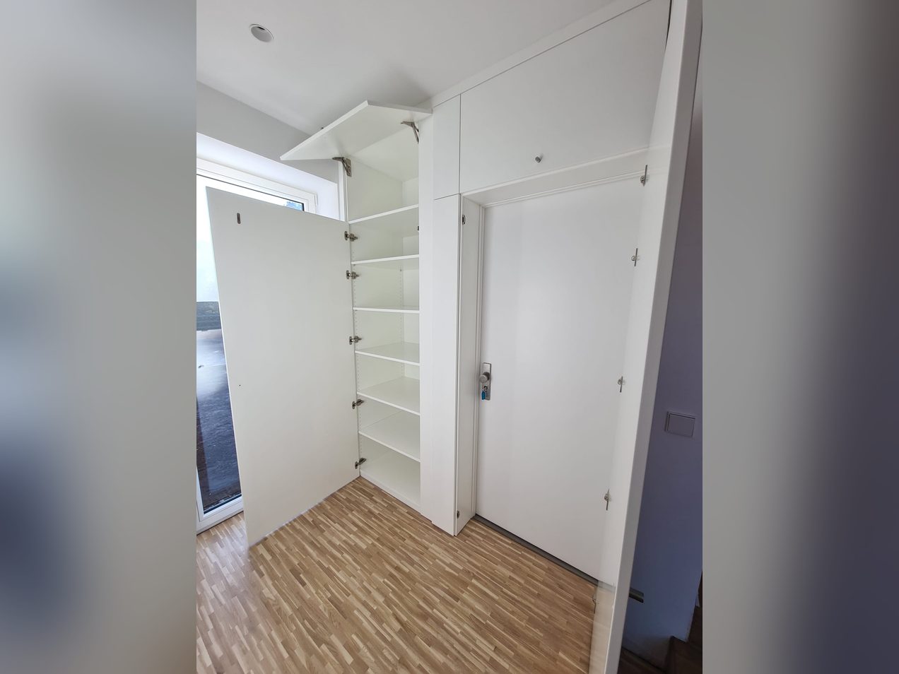 Geöffneter weißer Einbauschrank mit Regalböden, passgenau um eine Zimmertür gebaut