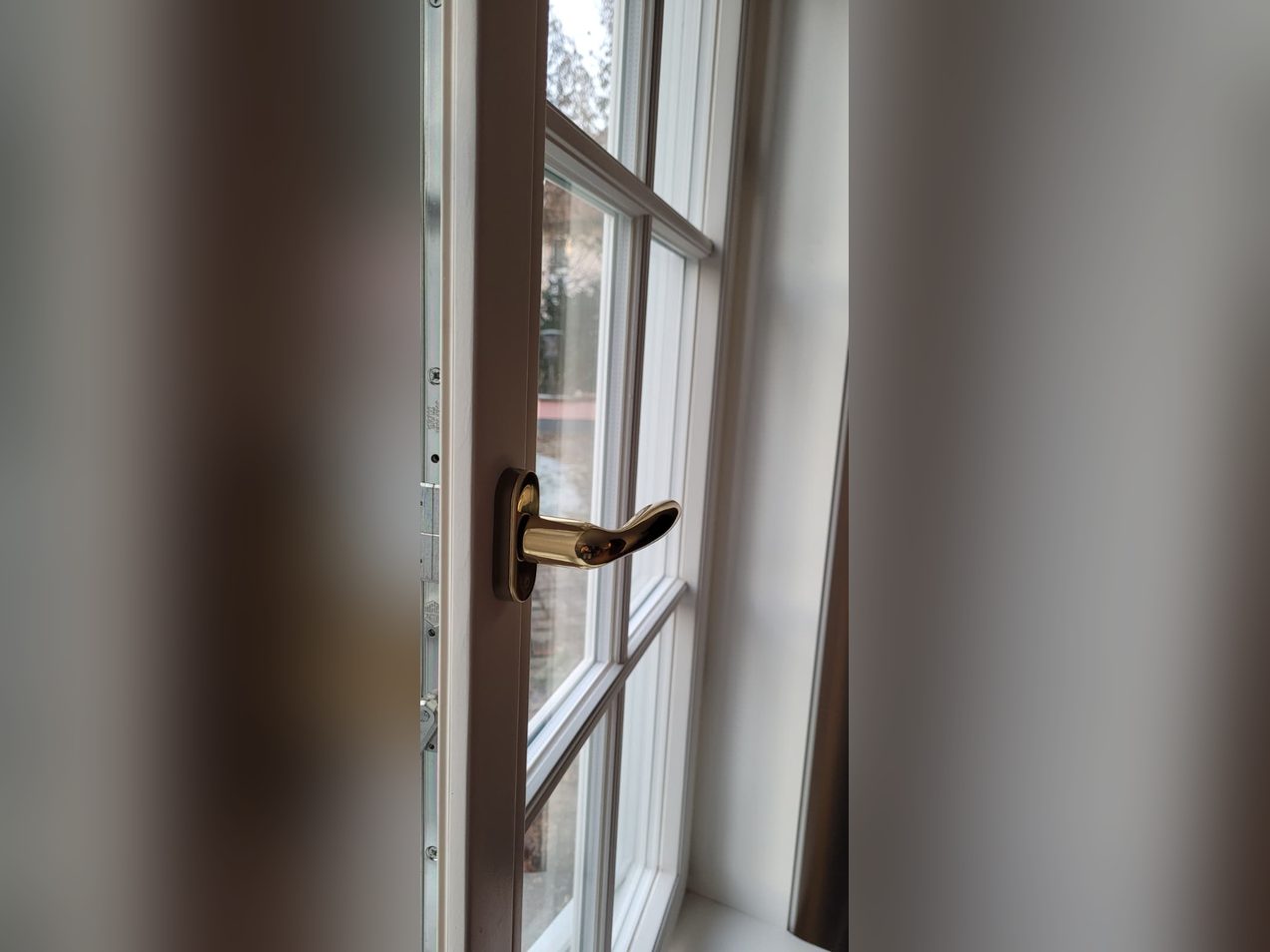 Detail eines weißen Holzfensters mit Sprossen und Messing-Fenstergriff