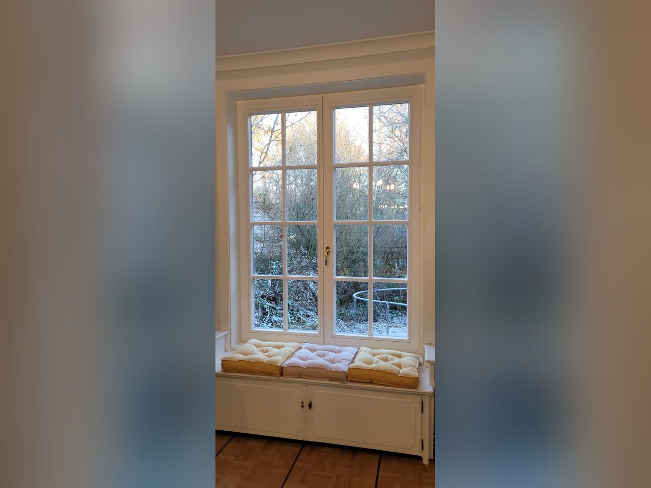 Weiße Holzfenster mit Sprossen über einer Fensterbank mit Sitzkissen