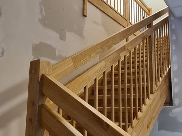 Holztreppe mit Handlauf und Stabgeländer aus Holz über zwei Etagen im Treppenhaus