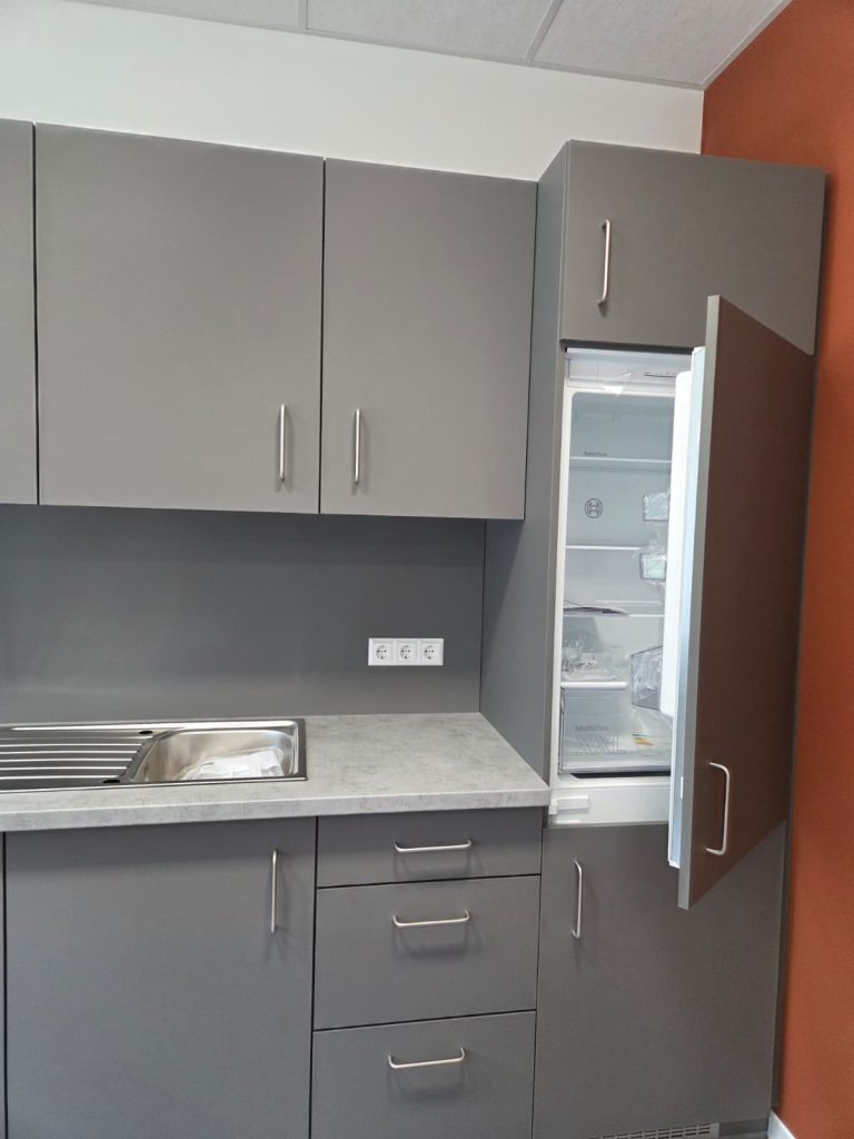 Grauer Küchenhochschrank mit integriertem Kühlschrank neben der Spüle