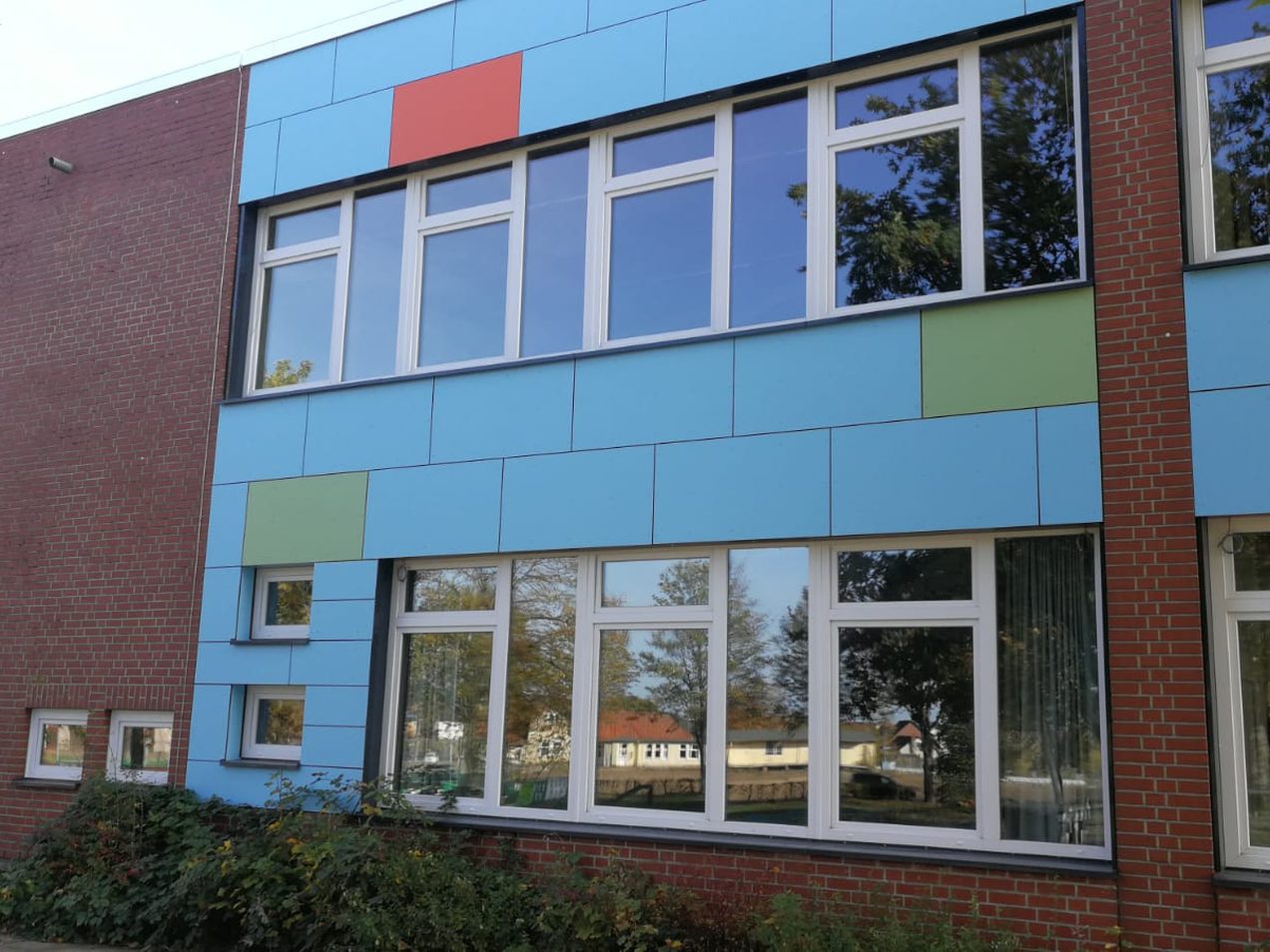 Weiße Kunststofffenster mit Oberlichtern in einer Schulfassade mit farbigen Paneelen