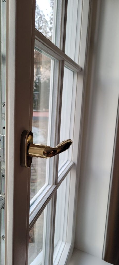 Detail eines weißen Sprossenfensters mit goldfarbenem Fenstergriff